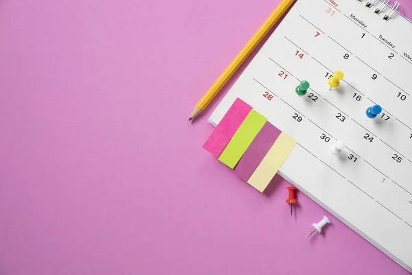 Крупним планом календар, олівець і шпилька на фоні рожевого столу — стокове фото