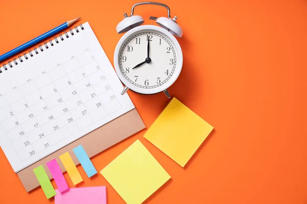 close up of alarm clock and calendar on the orange table background, planning for business meeting or travel planning concept