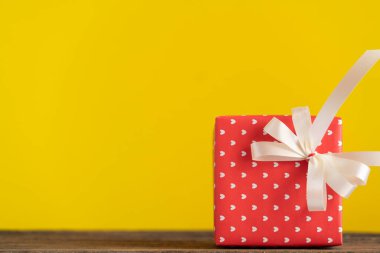 Ahşap masanın üzerinde sarı arka planı olan kırmızı hediye kutusu. 
