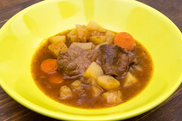 Stewed meat and vegetables on a wooden table seen close up