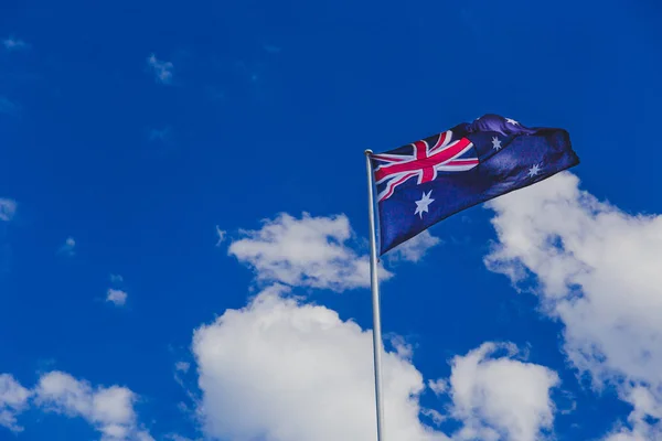 Australian flag waving in deep blue sky with fluffy clouds