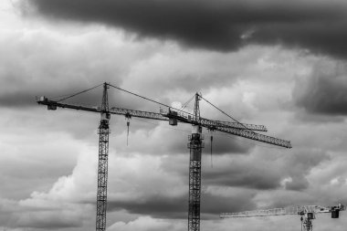 Üç İnşaat vinçleri üstlerindeki fırtınalı gökyüzü ile siyah ve beyaz kaldırıldı logoları ile vurdu.