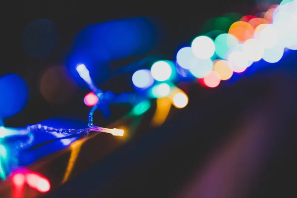 string of multicolored fairy lights on house terrace with bokeh effect and other street lights in the background