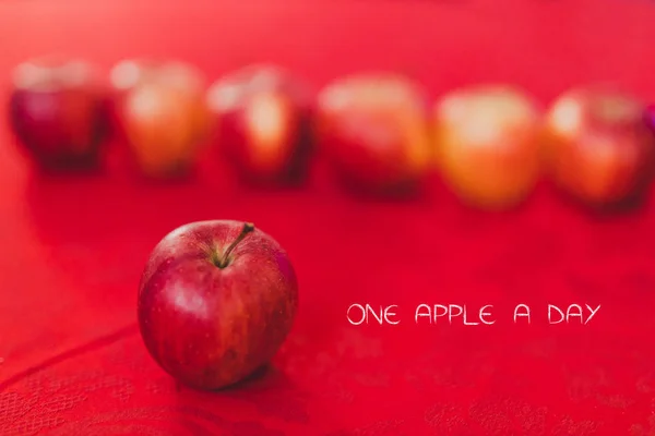 group of red apples on table cloth of the same color with text One a day