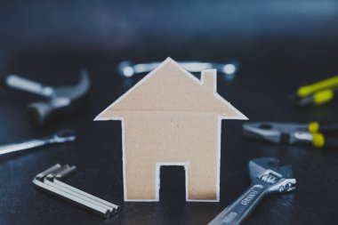 Bunu kendine ve ev yenileme kavramı: küçük ev kartondan yapılmış ve arka planda DIY araçları alan sığ derinlikte vurdu