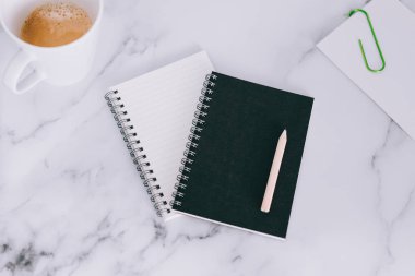 mini spiral defter kalem ile flatlay ve kahve mermer masa üzerinde yukarıdan aşağıya doğru perspektif vurdu