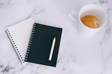 mini spiral defter kalem ile flatlay ve kahve mermer masa üzerinde yukarıdan aşağıya doğru perspektif vurdu