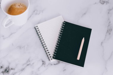 mini spiral defter kalem ile flatlay ve kahve mermer masa üzerinde yukarıdan aşağıya doğru perspektif vurdu