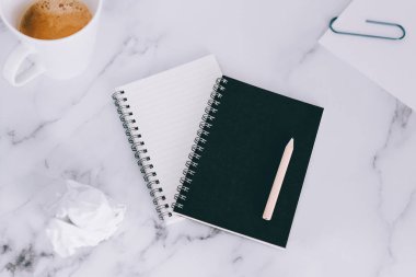 mini spiral defter kalem ile flatlay ve kahve mermer masa üzerinde yukarıdan aşağıya doğru perspektif vurdu