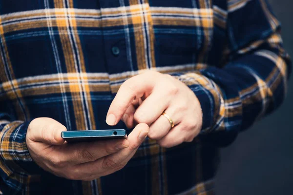 hipster man holding smartphone and tapping on the screen, focus on the hands and dark background