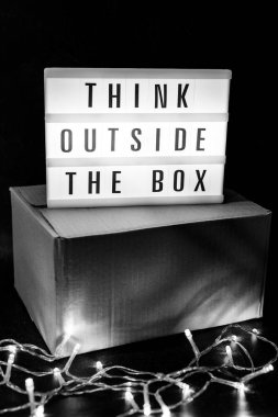 Think outside the box message on lightbox on top of closed parcel with fairy led lights, concept of being unique for success