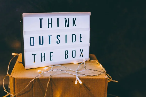 Think outside the box message on lightbox on top of closed parcel with fairy led lights, concept of being unique for success