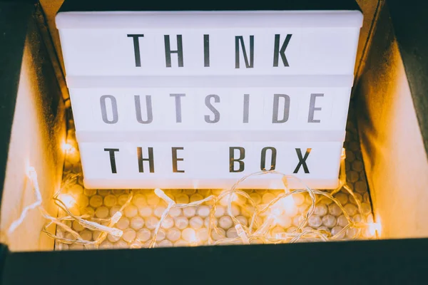 Think outside the box message on lightbox coming out of a parcel with fairy led lights, concept of being unique for success