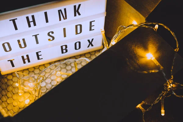 Think outside the box message on lightbox coming out of a parcel with fairy led lights, concept of being unique for success