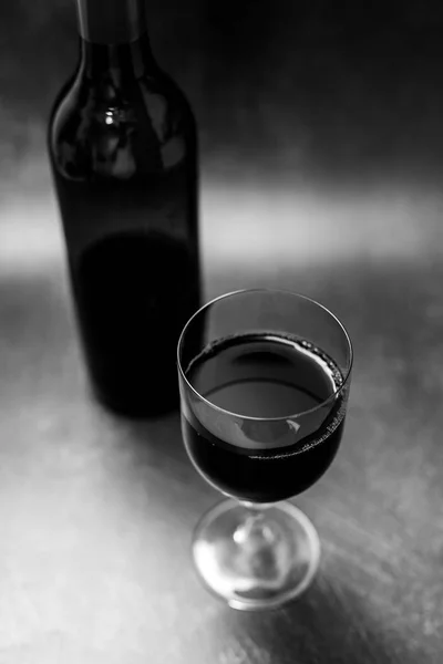 glass of intensely coloured red wine and bottle on dark background, concept of elegant or expensive wine choices