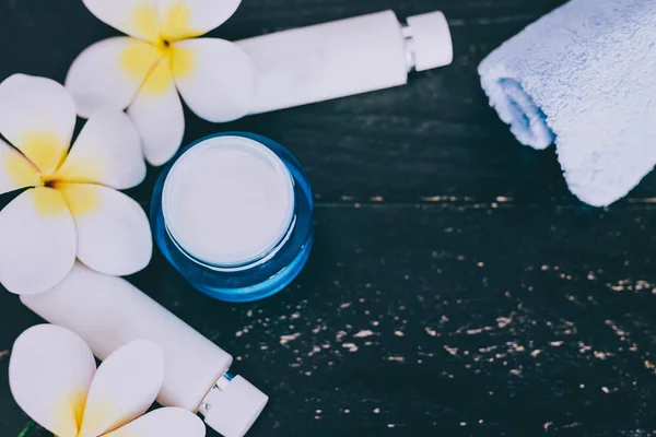 mixed skincare and beauty products with flowers and seashells on dark wood background, concept of luxury spa and pampering