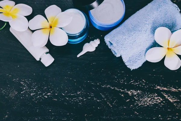 mixed skincare and beauty products with flowers and seashells on dark wood background, concept of luxury spa and pampering