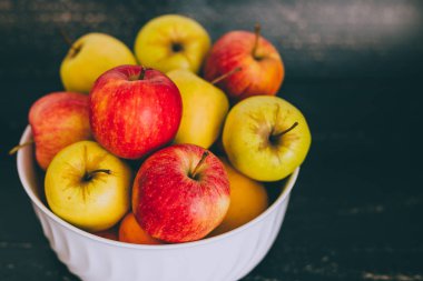 Grup koyu ahşap arka plan, organik ürünler ve plentiness kavramı üzerinde beyaz bir kase karışık kırmızı yeşil ve Sarı elmalar