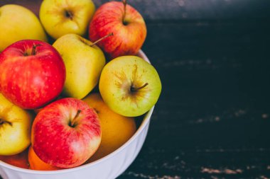 Grup koyu ahşap arka plan, organik ürünler ve plentiness kavramı üzerinde beyaz bir kase karışık kırmızı yeşil ve Sarı elmalar