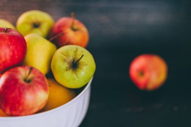 Grup koyu ahşap arka plan, organik ürünler ve plentiness kavramı üzerinde beyaz bir kase karışık kırmızı yeşil ve Sarı elmalar