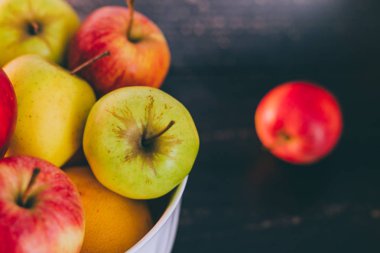 Grup koyu ahşap arka plan, organik ürünler ve plentiness kavramı üzerinde beyaz bir kase karışık kırmızı yeşil ve Sarı elmalar