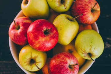 Grup koyu ahşap arka plan, organik ürünler ve plentiness kavramı üzerinde beyaz bir kase karışık kırmızı yeşil ve Sarı elmalar