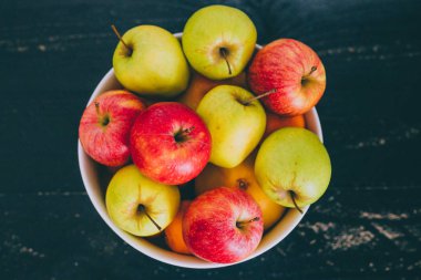 Grup koyu ahşap arka plan, organik ürünler ve plentiness kavramı üzerinde beyaz bir kase karışık kırmızı yeşil ve Sarı elmalar