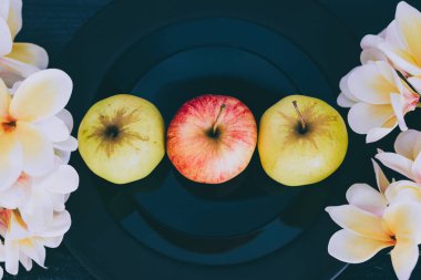 siyah plaka en iyi organik ürünler seçme kavramı koyu arka plan ve çevrelerindeki beyaz çiçekler üzerinde yeşil ve kırmızı elma