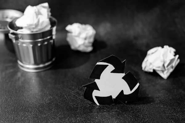 recycle symbol surrounded by scrunched paper balls with garbage bin, concept of reducing damage to the environment