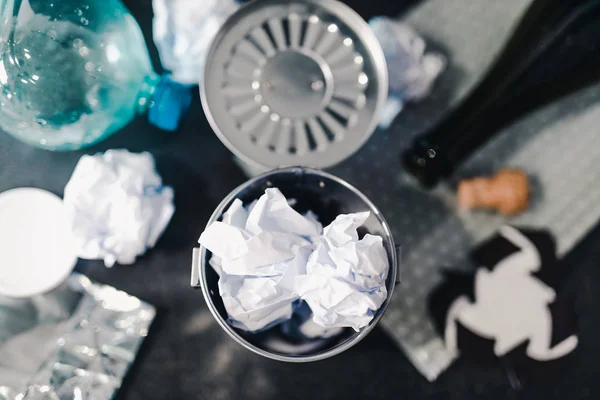 full trash can surrounded by reusable waste materials like plastic paper and glass with recycle symbol, concept of reducing damage to the environment