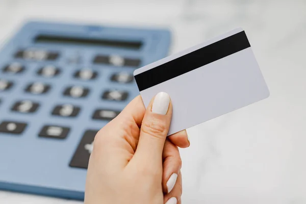 woman\'s hand holding payment card in front of huge calculator, concept of shopping budget