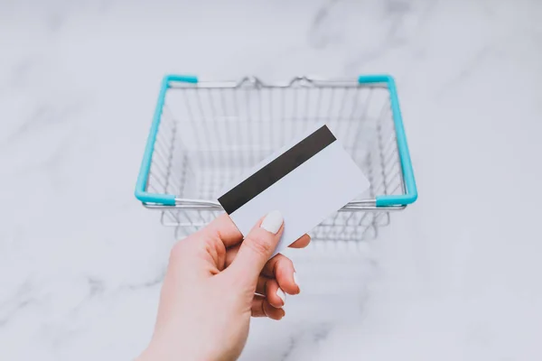 woman\'s hand holding payment card in front of empty shopping basket, concept of shopping budget