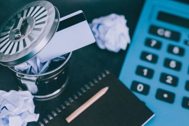 ödeme kartı büyük hesap makinesi ve Not defteri, daha az harcamak öğrenme kavramı yanındaki çöpe atılan ve bir bütçe sadık