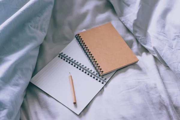 empty notepads with copyspace and pencil on messy bed sheets, concept of working from home or making plans in the morning