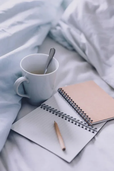 empty notepads with copyspace and pencil on bed with mug of coffee next to it, concept of starting the morning and writing a schedule or to do list