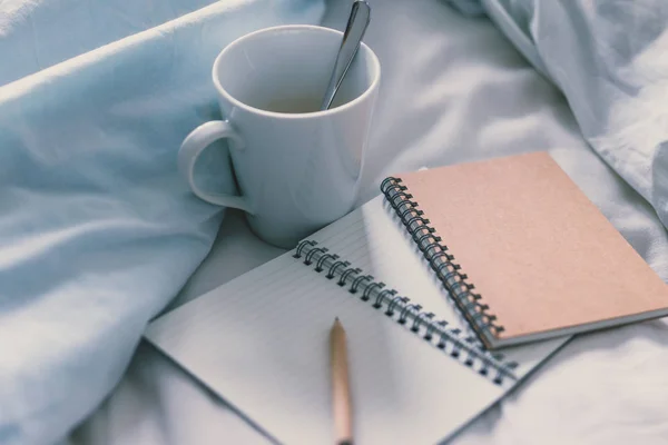 empty notepads with copyspace and pencil on bed with mug of coffee next to it, concept of starting the morning and writing a schedule or to do list