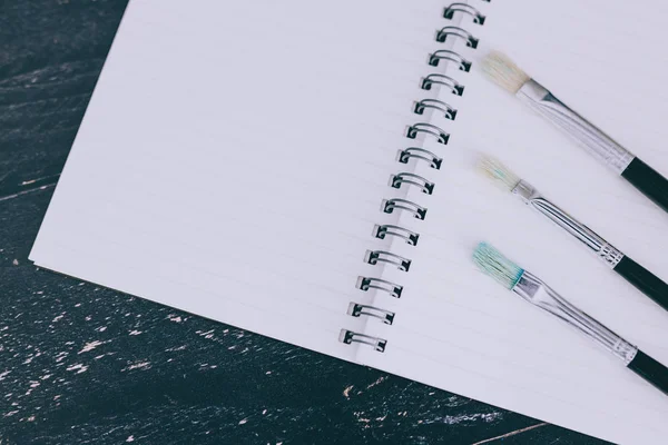 Desk with notepads and watercolour brushes with empty pages and — Stock Photo, Image