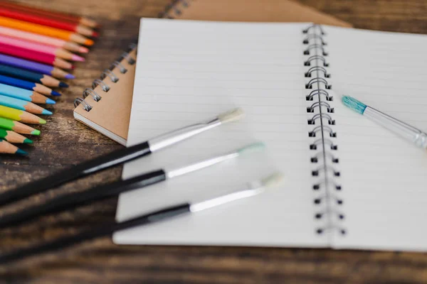 Cuaderno con pinceles y lápices de color en escritorio de madera — Foto de Stock