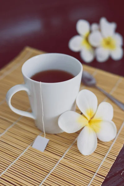Cup of dark tea on bamboo placemat with spoon and flowers all ar — Stock Photo, Image