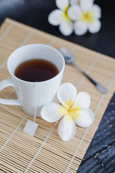 Secangkir teh hitam di piring bambu dengan sendok dan bunga semua ar — Stok Foto