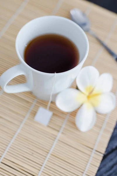 Tasse de thé noir sur napperon en bambou avec cuillère et fleurs tous ar — Photo