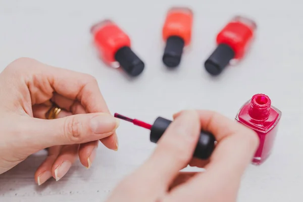 Manos de mujer con botella de esmalte de uñas rojo y otros colores en wo — Foto de Stock