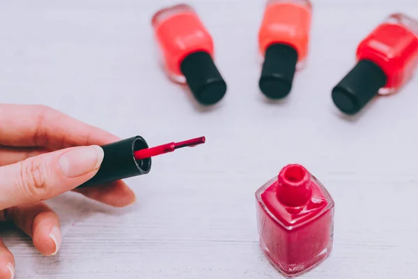 Manos de mujer con botella de esmalte de uñas rojo y otros colores en wo — Foto de Stock