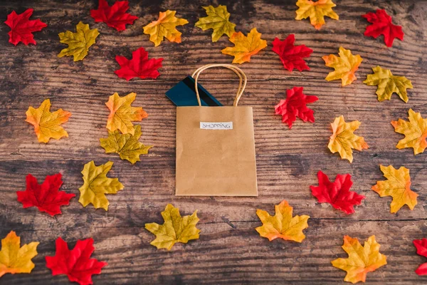 Shopping bag on wooden table surrounded by autumn leaves, — Stock Photo, Image
