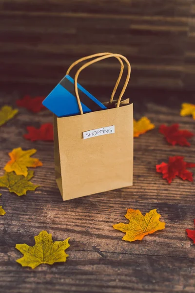 Shopping bag with payment card on wooden table surrounded by aut — Stock Photo, Image