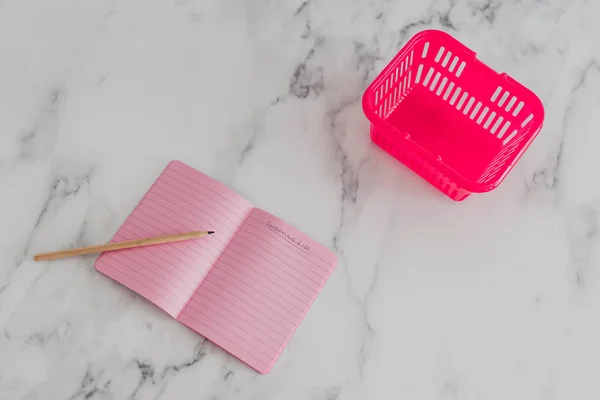Różowy koszyk na biurko z marmuru z listą na notebooku — Zdjęcie stockowe