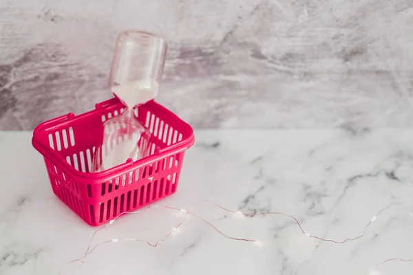 Růžový nákupní košík se konceptem přesýpacích hodin — Stock fotografie