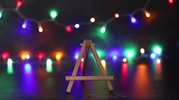 Hand Platziert Leere Leinwand Miniatur Vor Bunten Festlichen Lichterketten Bokeh — Stockvideo