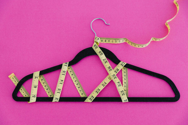 clothes hanger with measuring tape on pink background