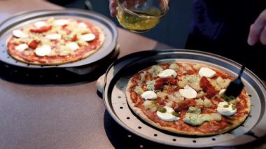 Genç adam evde ev yapımı vejetaryen pizza yapıyor. Üstüne pesto sosu ekliyor.
